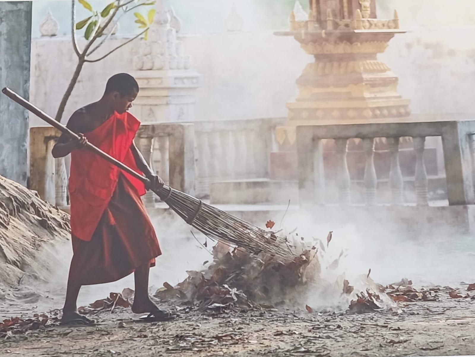 Moine en robe orange balayant une cour de temple, image du lâcher-prise face au stress
