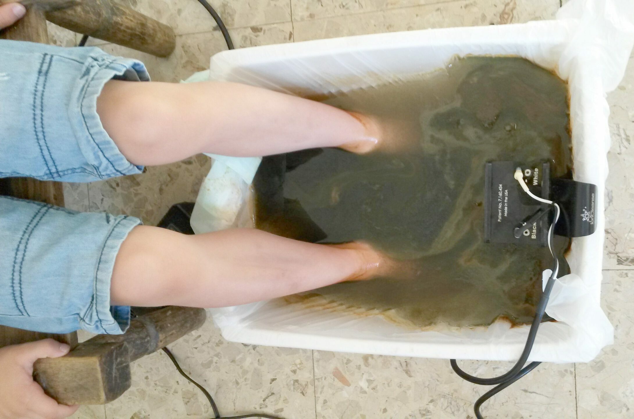 Bain de pieds ionique : pieds plongés dans une bassine d'eau avec l'appareil de détoxination